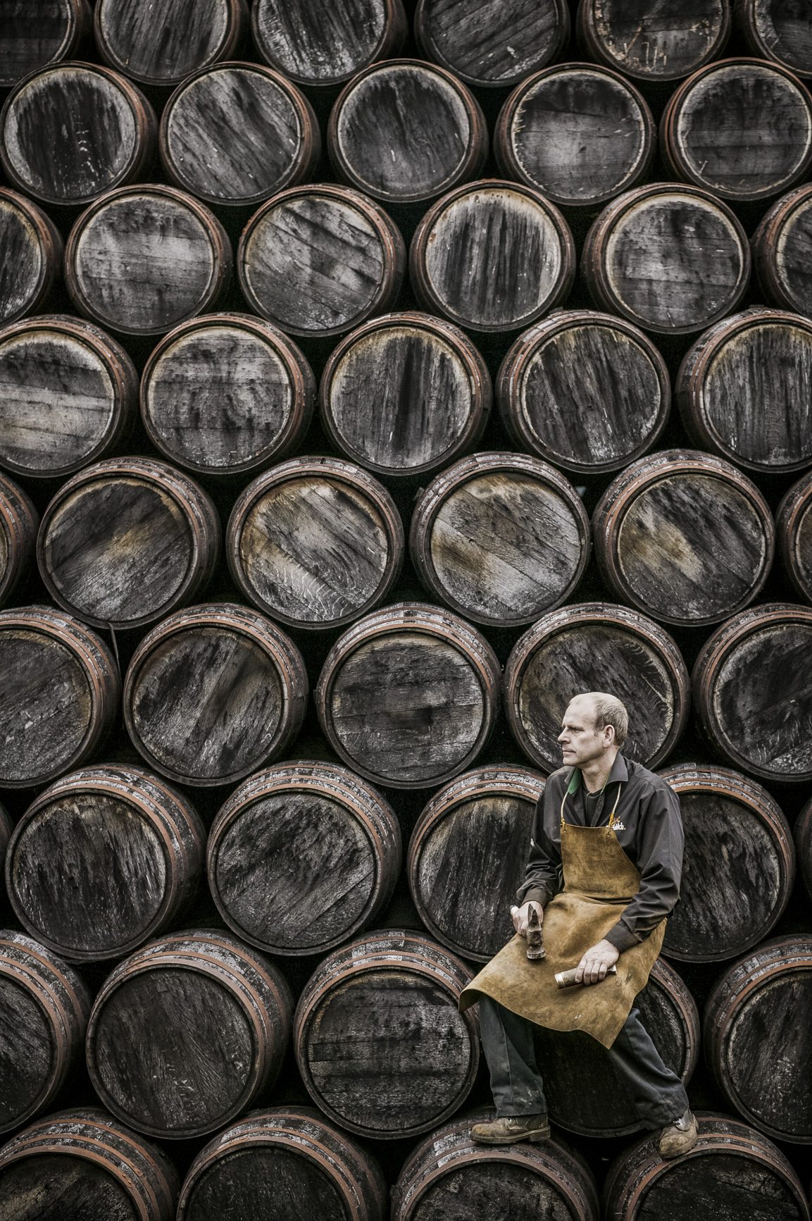 A cooper resting against a wall of stacked whisky casks